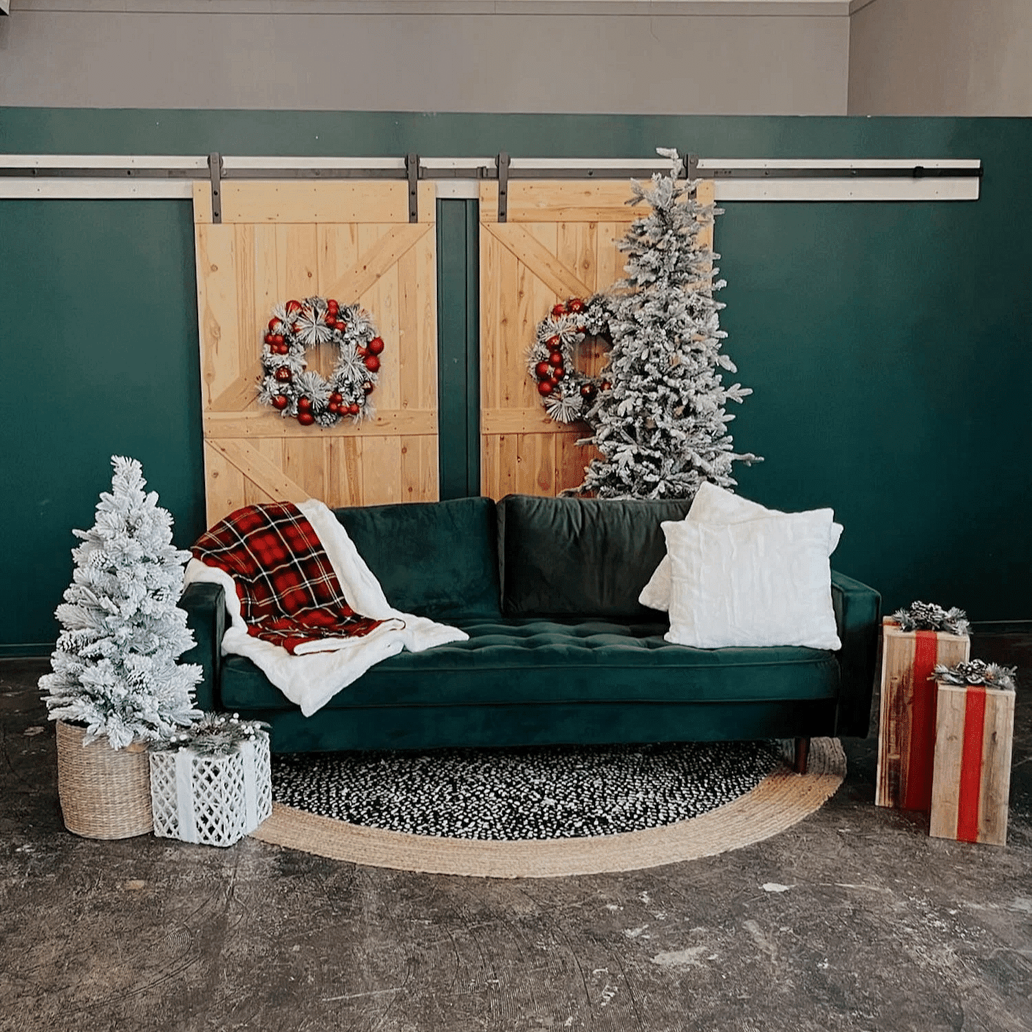 Green couch with white pillows, plaid blanket, and holiday decor including wreaths and small trees.