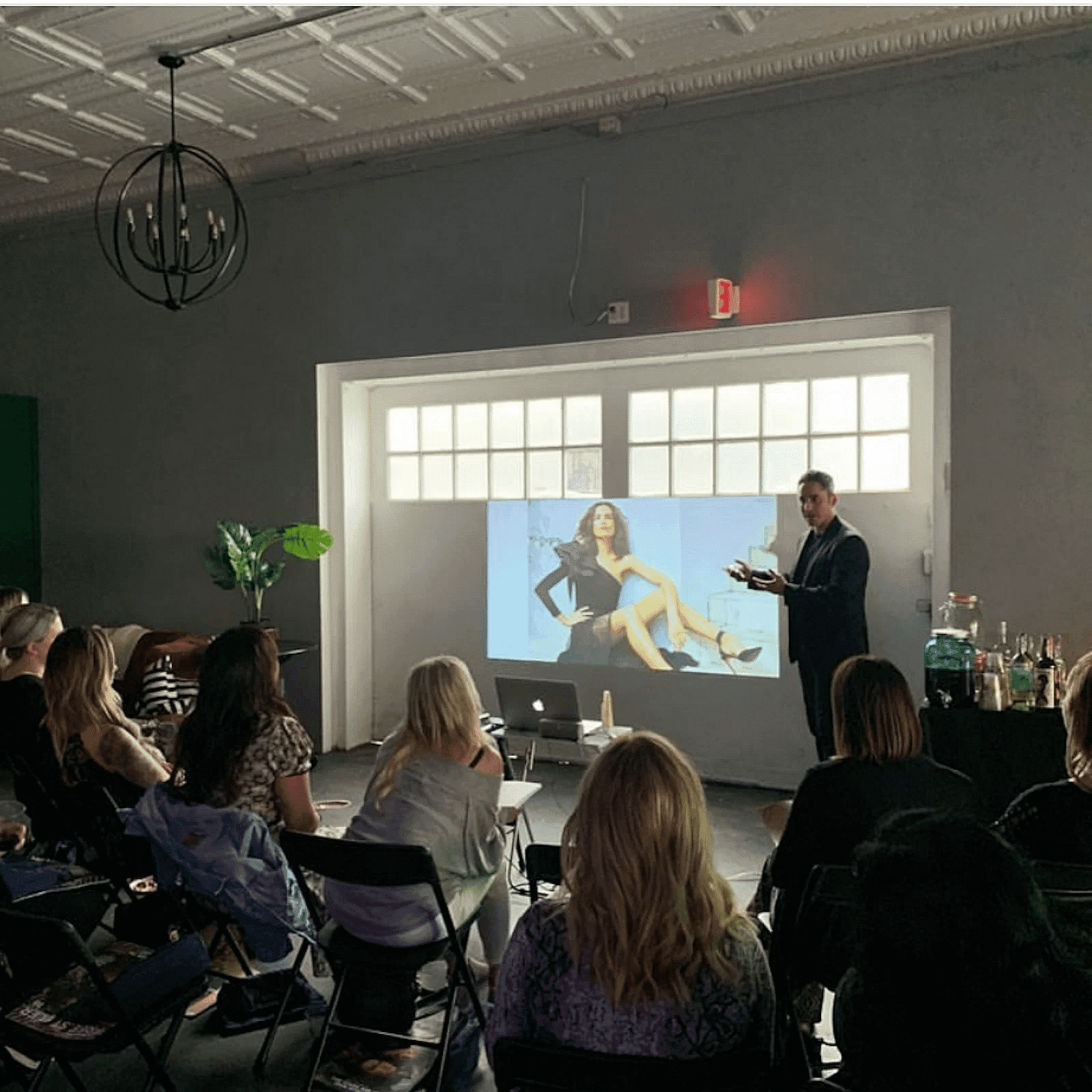 Man presenting to a seated audience with a large photo of a woman projected on the screen.